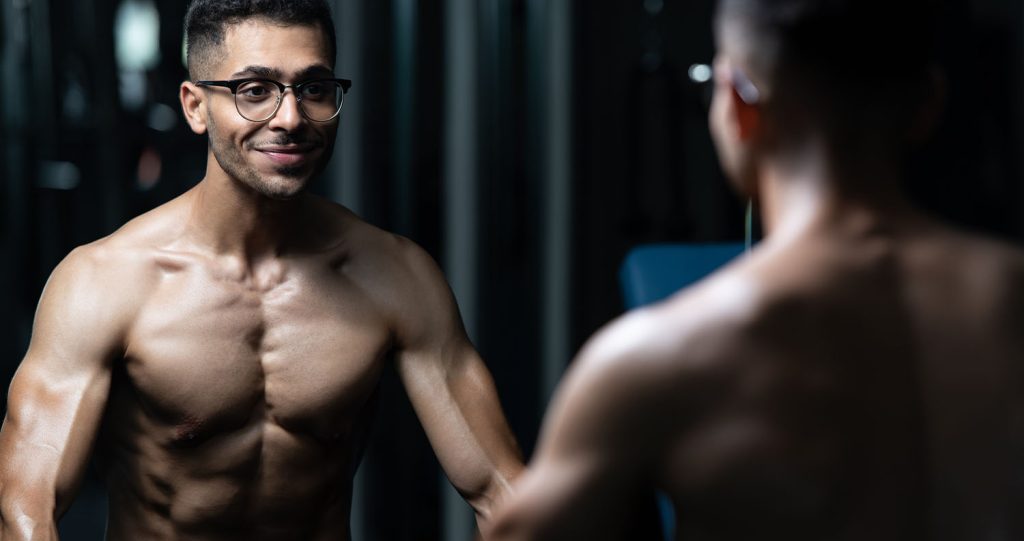Bodybuilder with gynecomastia flexing muscles in front of a mirror