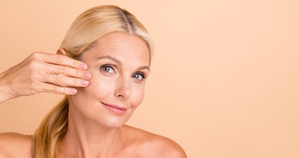 Mature woman after facelift gently touches her face (model)